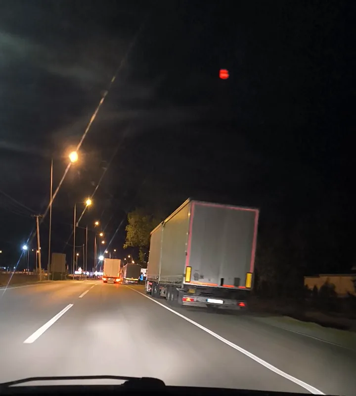 A lit road at night with lorries queued along the right-hand side, seen through a car windscreen