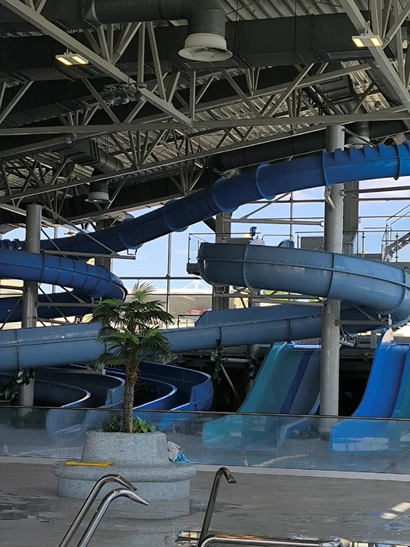 Indoor water slides behind a glass barrier and a small round pool with steel handrails in the foreground