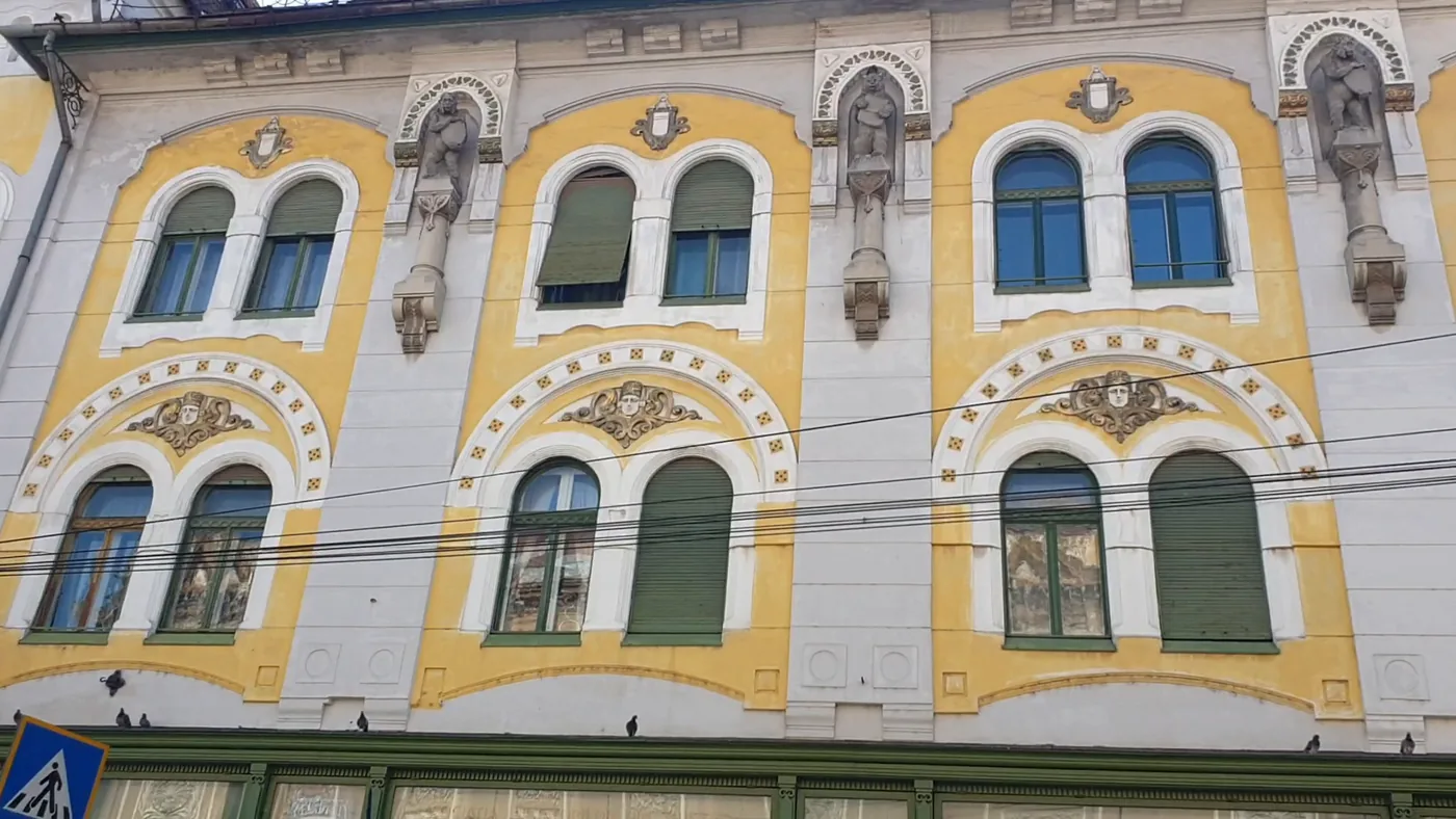 Close view of a yellow and white Secession facade with tall arched windows and sculpted figures between them