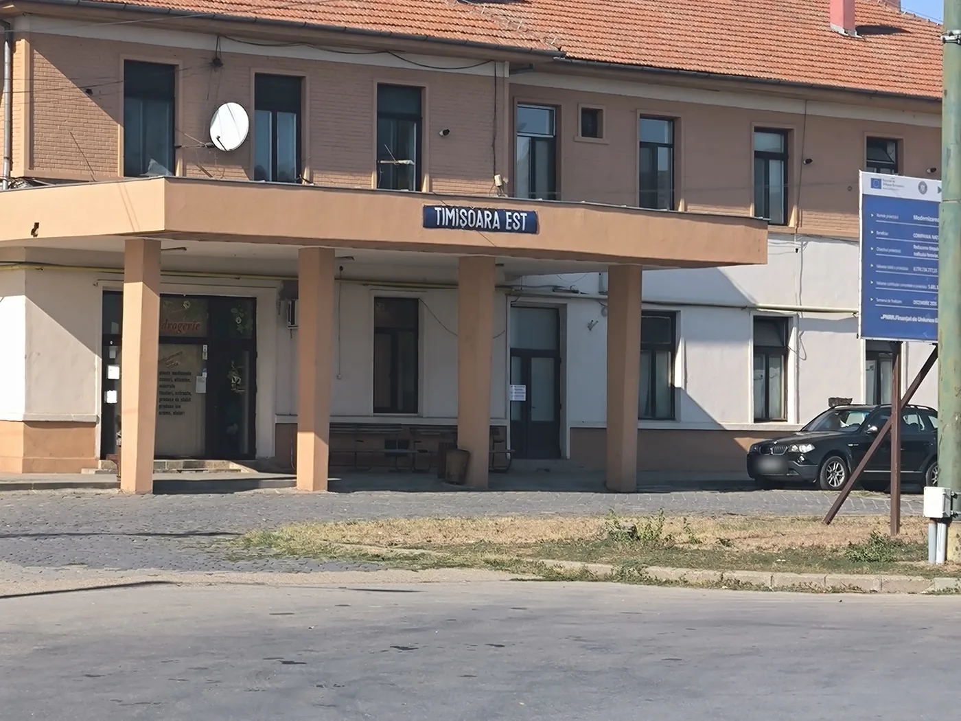 The entrance canopy of a station building with the sign Timisoara Est, a parked car beside it