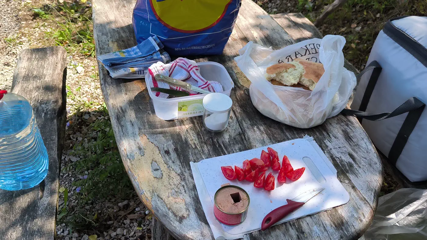 Breakfast on a wooden picnic table by the Danube: sliced tomatoes, tinned pate, bread and a cool bag